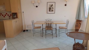 A dining area with a table and chairs, a kitchen with cabinets, and a wall-mounted air conditioner. - apartment with little garden five minutes walk from the beach (Trinità DAgultu e Vignola)