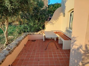 A patio with a table and benches, surrounded by greenery and a stone wall. - apartment with little garden five minutes walk from the beach (Trinità DAgultu e Vignola)