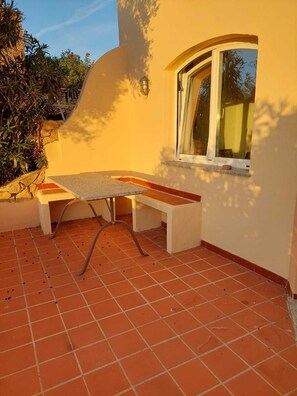 A patio area with a table and benches, a window, and a tiled floor. - apartment with little garden five minutes walk from the beach (Trinità DAgultu e Vignola)