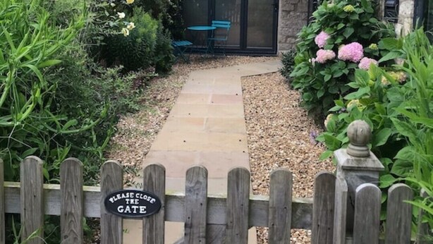 A stone building with a glass door, surrounded by a wooden fence and a pathway leading to a gate.