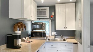 A modern kitchen with white cabinetry, a built-in microwave, a coffee maker, and a sink. - Cozy Condo with Views of Mt Kineo (Rockwood)
