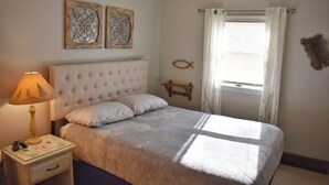 A bedroom with a tufted headboard, a bed with white bedding, a bedside lamp, a nightstand with a lamp, and two wall-mounted decorative pieces. - Cozy Condo with Views of Mt Kineo (Rockwood)