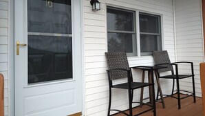 A porch with two chairs and a table, a door with a brass handle, and a window with a lantern above it. - Cozy Condo with Views of Mt Kineo (Rockwood)