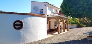 A white building with a tiled roof, a circular window, and an outdoor patio area with a table and chairs. - Beautiful Rustic Villa with Private Pool overlooking Spectacular Mountain Views (Cártama)