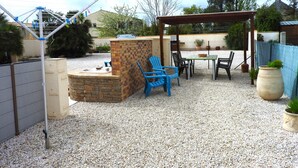 Un patio con una parrilla, mobiliario y una pérgola.