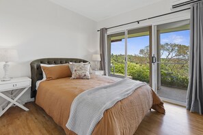 A bedroom with a large bed, a nightstand, a lamp, and a view of greenery through a sliding glass door. - Luxurious Scenic Escape in Maleny  (Maleny)