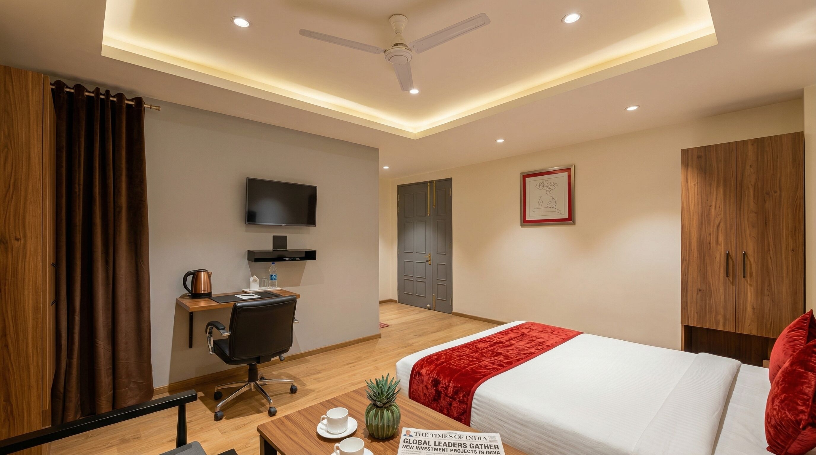 Ein Hotelzimmer mit Bett, Schreibtisch, Stuhl, Fernseher, Kleiderschrank und Deckenventilator.