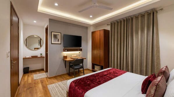 A hotel room with a bed, desk, chair, television, wardrobe, and a ceiling fan.