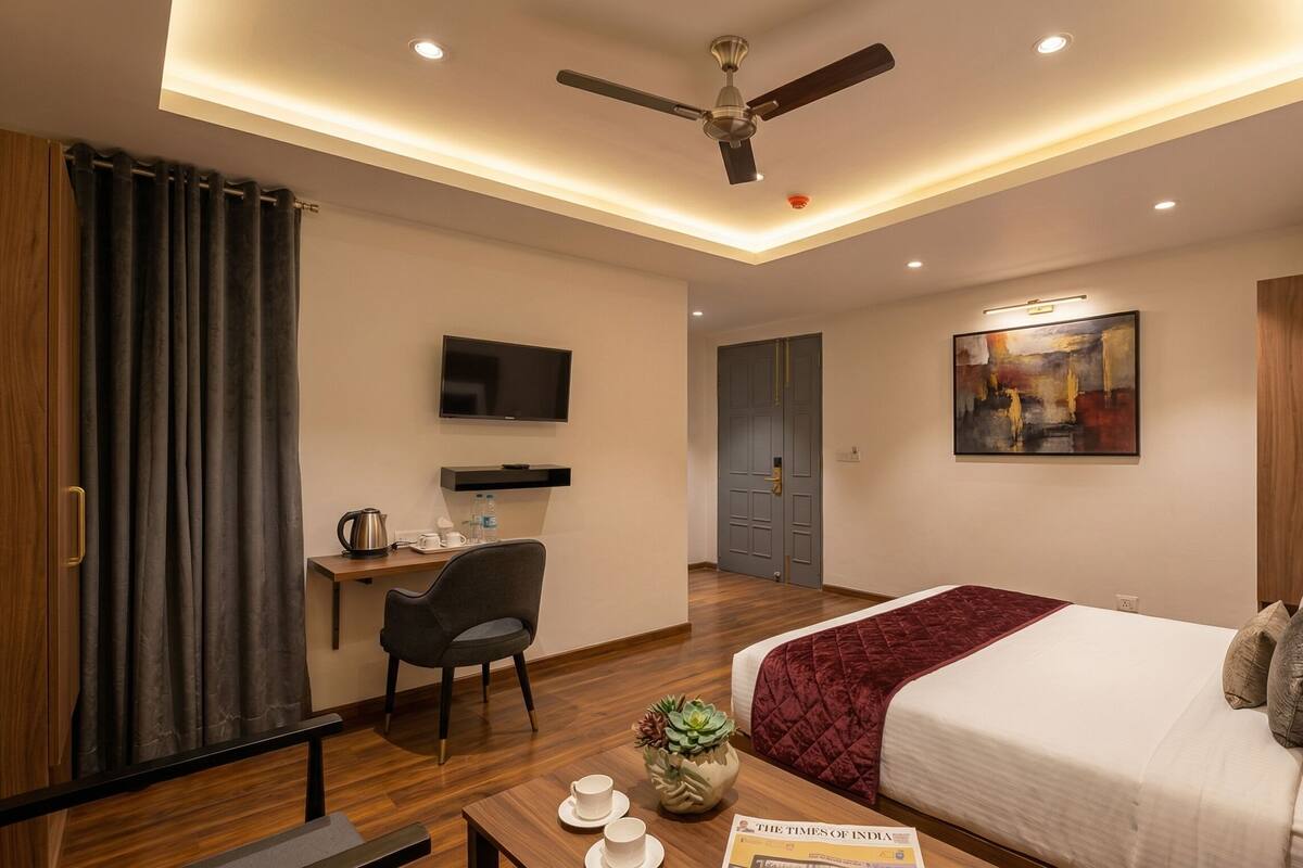 A modern hotel room with a bed, desk, chair, TV, artwork, and a ceiling fan.