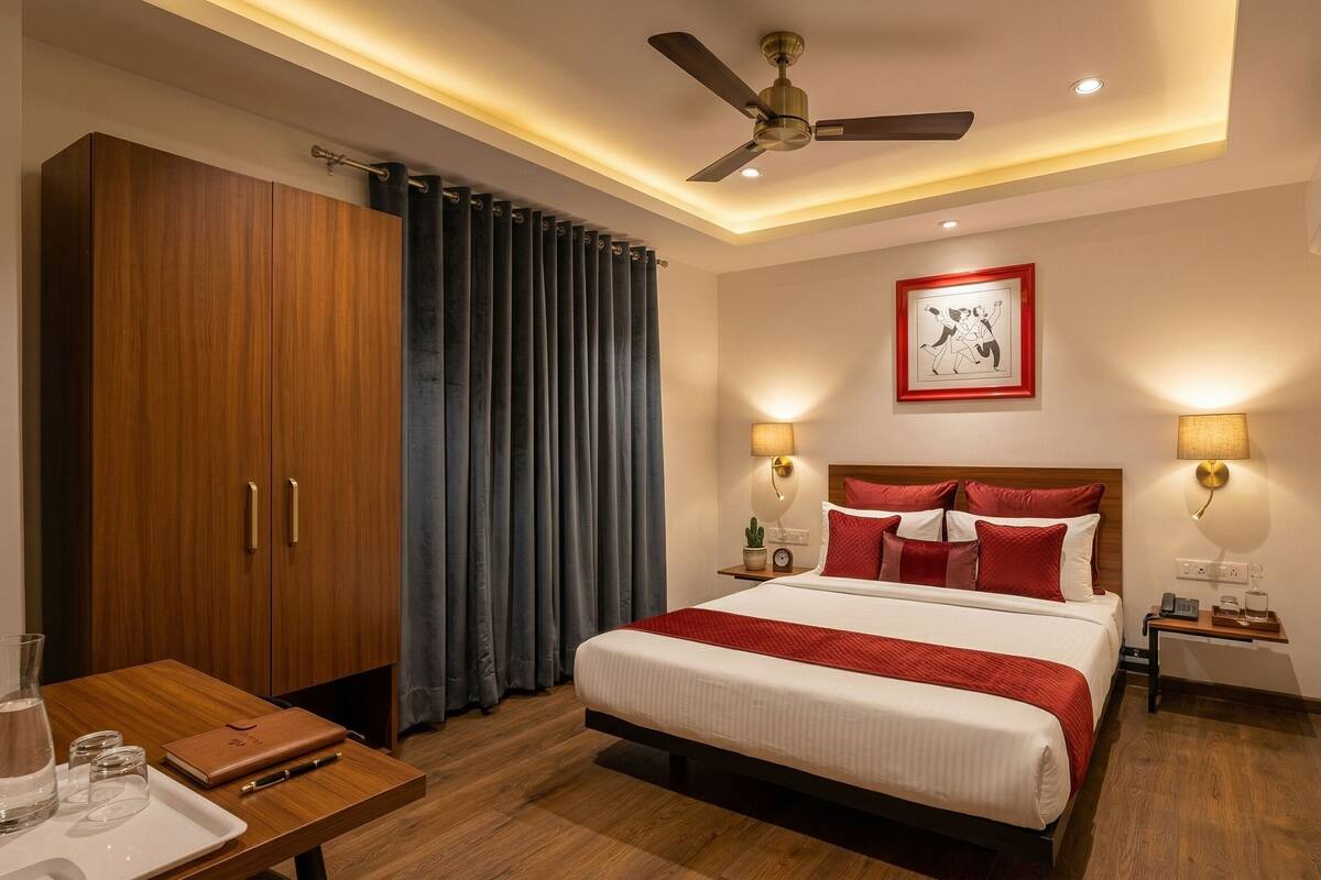 A hotel room with a bed, bedside tables, a desk, a ceiling fan, and an air conditioning unit.