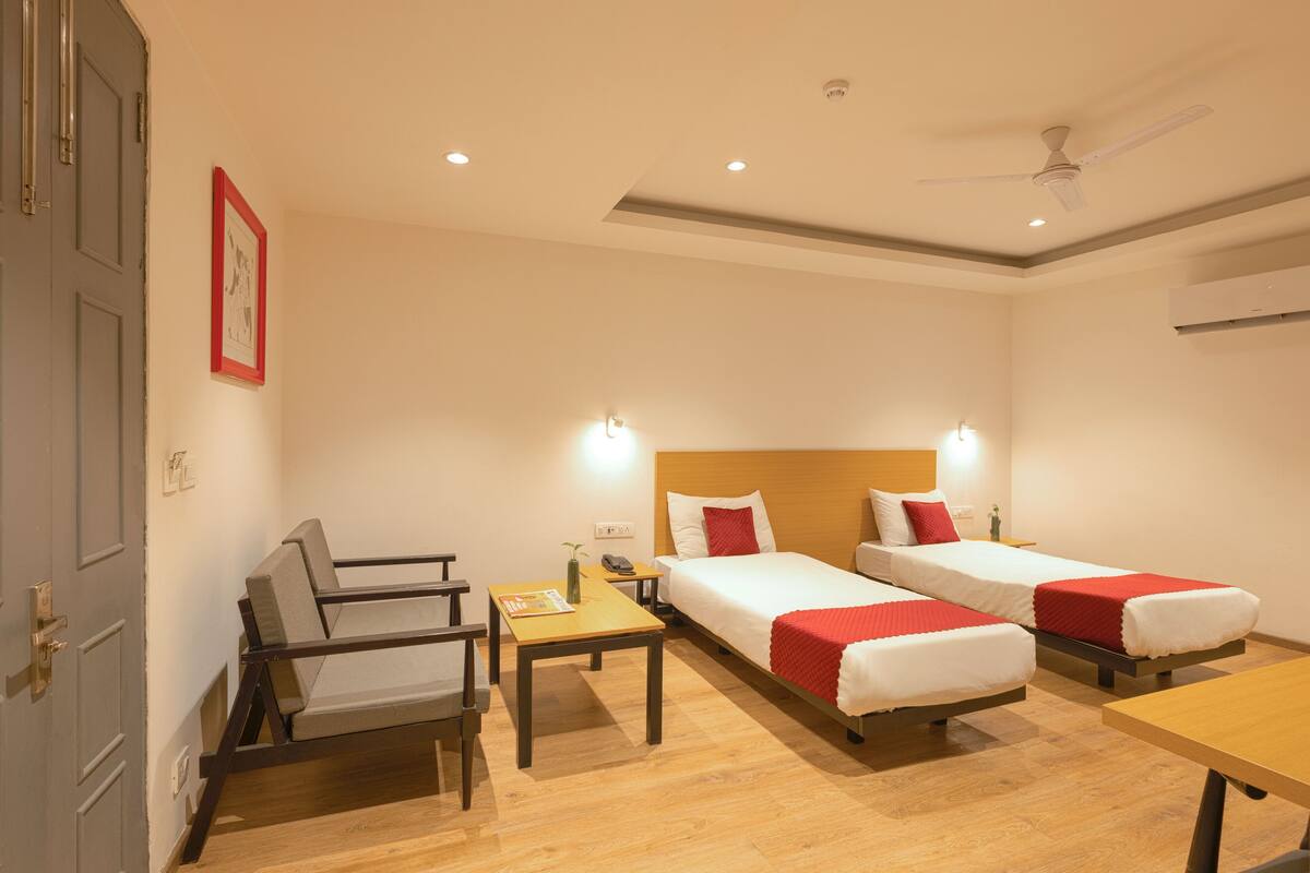 A hotel room with two single beds, a desk, a chair, a table, and a ceiling fan.