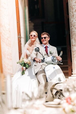 A wedding couple on a scooter, with a building in the background.