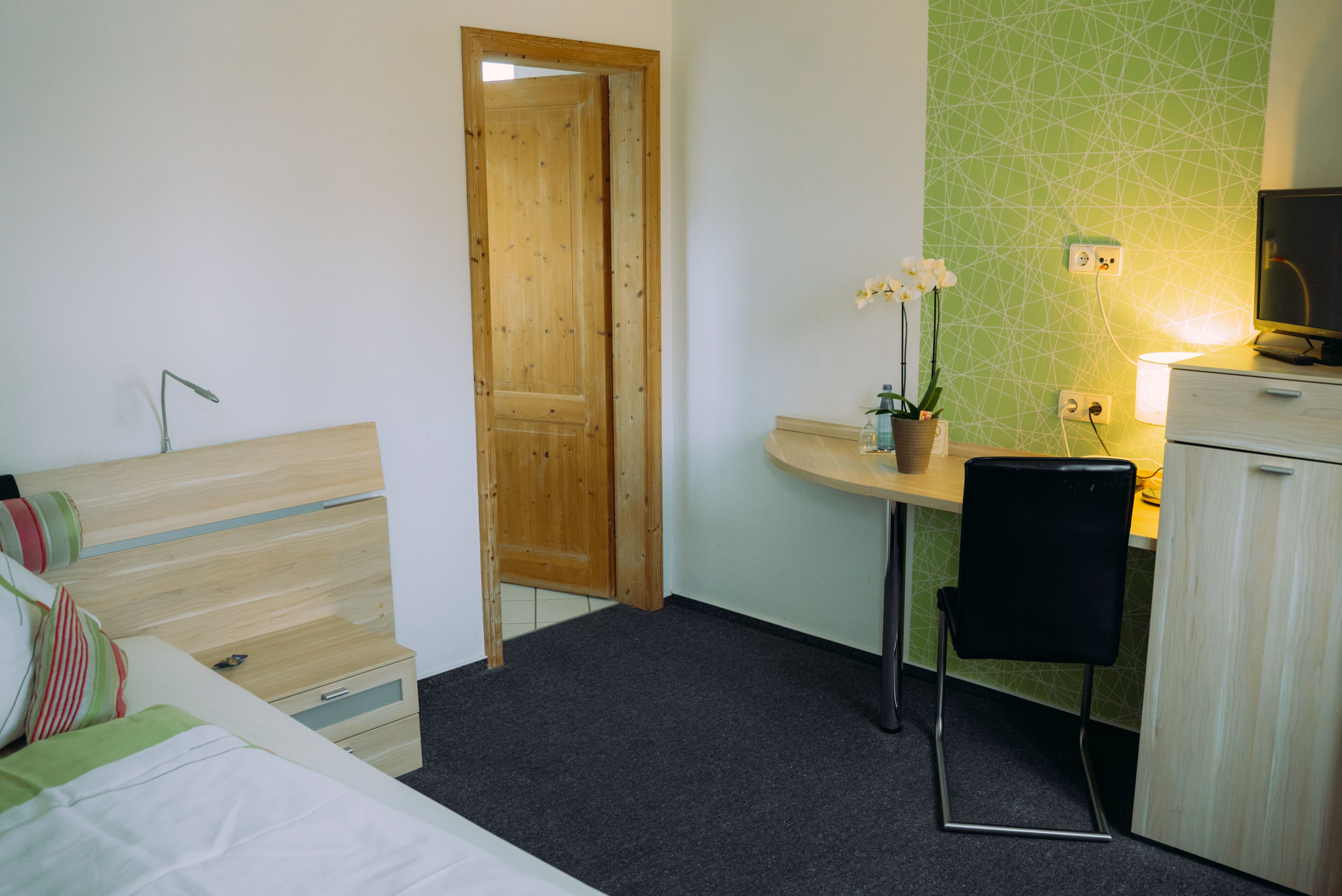 A bedroom with a bed, a desk, a chair, a television, and a small potted plant.