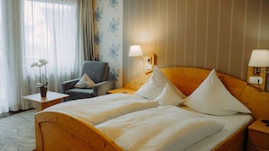 Een hotelkamer met een houten bed, een stoel, een tafeltje met een lamp en bloemenbehang.