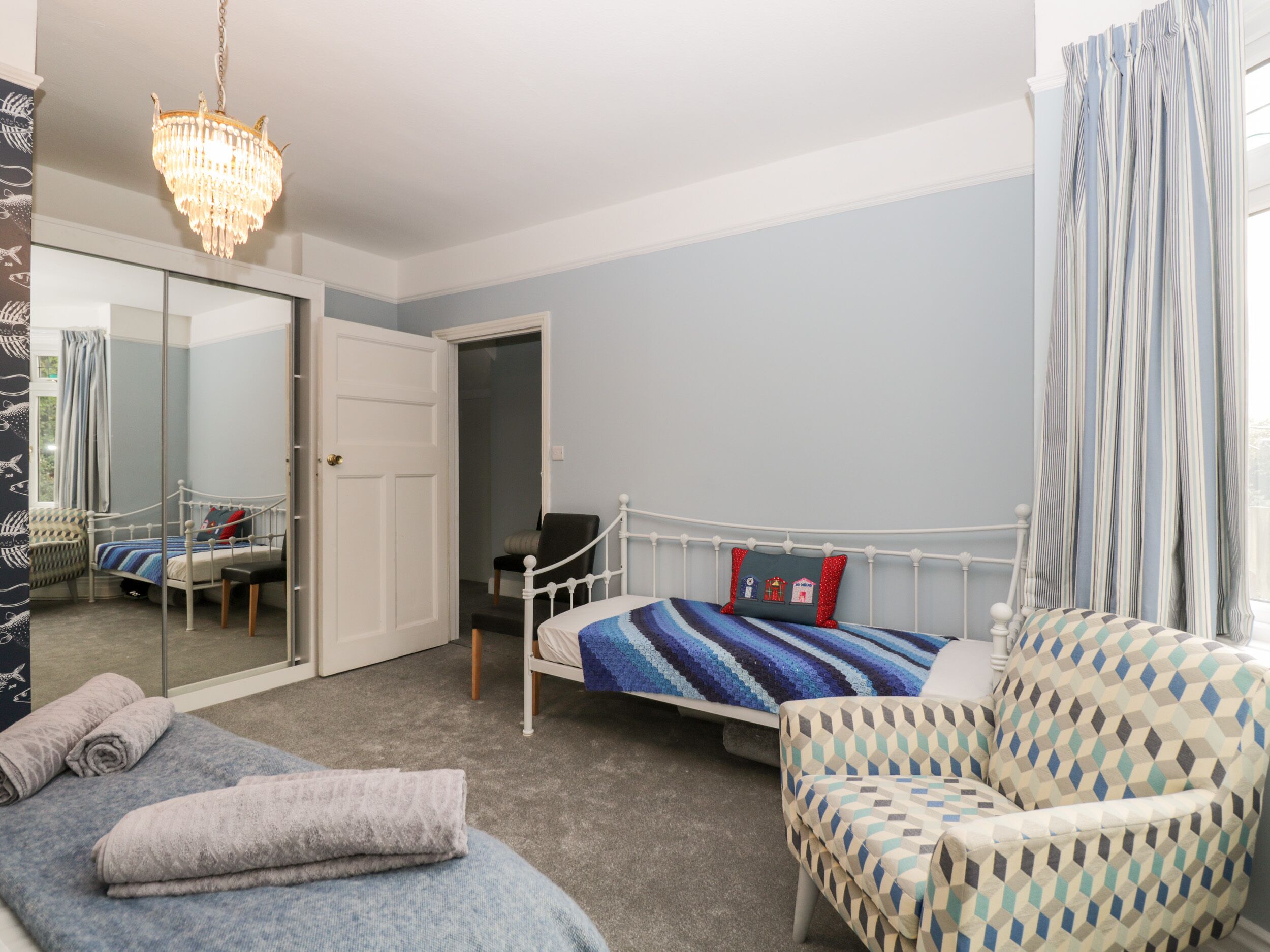 A bedroom with a bed, a chair, a mirror, and a chandelier.