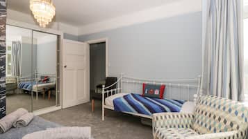 A bedroom with a bed, a chair, a mirror, and a chandelier.