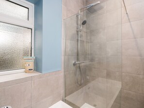 Une douche avec une porte en verre, une fenêtre à carreaux dépolis et un petit tabouret en bois.