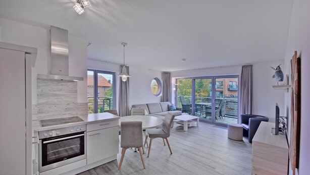 Eine moderne Küche mit Einbauofen, Essbereich mit rundem Tisch und Stühlen sowie ein Wohnzimmer mit Sofa und Fernseher.