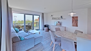 Ein modernes Wohnzimmer mit einer Couch, einem Esstisch und Stühlen. Es gibt einen Balkon mit Gartenmöbeln.