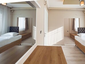 A modern hotel room with a wooden floor, two beds with headboards, a wooden bench, and a large mirror.