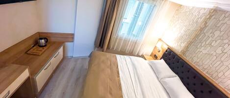 Una habitación de hotel con cama, una mesita de noche de madera, una lámpara y vistas a la ciudad desde la ventana.