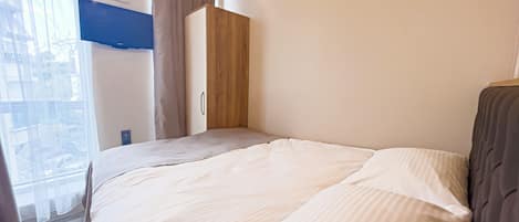 Un dormitorio con cama, armario y ventana con cortinas.