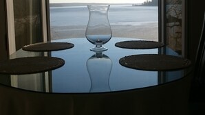 Ein Tisch mit einer Glasvase und zwei Platzsets, ein Fenster mit Blick auf Strand und Wasser.