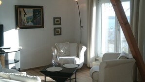 Ein geräumiges Wohnzimmer mit hoher Decke, einem Holzbalken, einem weißen Sofa, einem Couchtisch und einem Gemälde an der Wand.