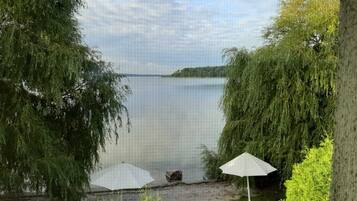 Blick auf einen See mit einer grünen Wiese, einem weißen Sonnenschirm und üppiger Vegetation.