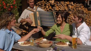 En grupp människor sitter vid ett träbord utomhus och njuter av mat och dryck.