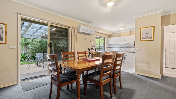 A dining area with a wooden table and chairs, a kitchen with white cabinets, and a sliding glass door leading to an outdoor patio.