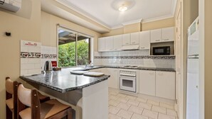 A modern kitchen with white cabinets, a granite countertop, a built-in oven, a microwave, and a refrigerator.