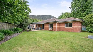 A single-story brick house with a covered patio, a lawn, and a wooden fence.