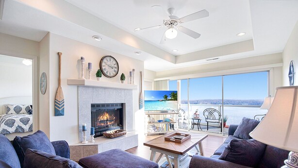 A modern living room with a fireplace, comfortable seating, a large window with a view, and a ceiling fan. - Upscale Condo, Amazing Views, Pools and Pickleball (Lake Ozark)
