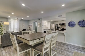 Cozinha moderna com armários brancos, eletrodomésticos de aço inoxidável e um espaço de refeições com mesa e cadeiras de madeira.