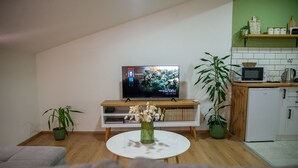 Ein Wohnzimmer mit Fernseher, weißem Couchtisch, einer Couch und zwei Zimmerpflanzen.