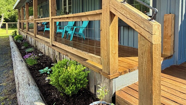 Un porche cubierto con barandillas de madera, mobiliario exterior y una planta en maceta.