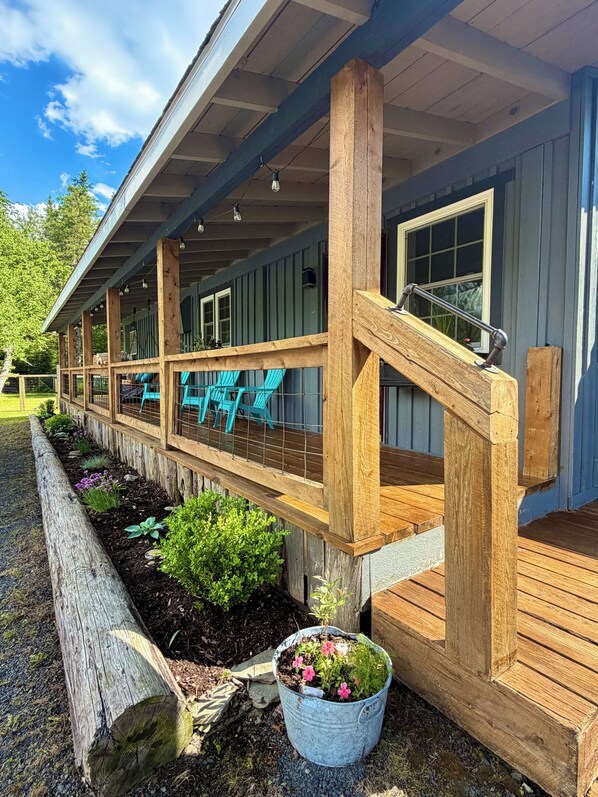 A covered porch with wooden railings, outdoor seating, and a potted plant.