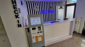 A hotel reception area with a self-check-in kiosk, a neon sign, a clock, and a window with a view. - HOTEL NORTE (Zarautz)