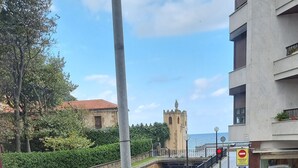 A view of a coastal street with a castle-like structure in the background, a pedestrian crossing, and a building with a balcony. - HOTEL NORTE (Zarautz)