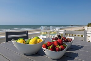 Une table avec des corbeilles de fruits et deux verres de vin blanc, donnant sur une plage.