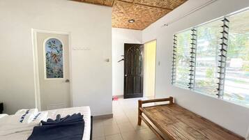 A room with a bed, a bench, a door with a decorative window, and a large window with blinds.