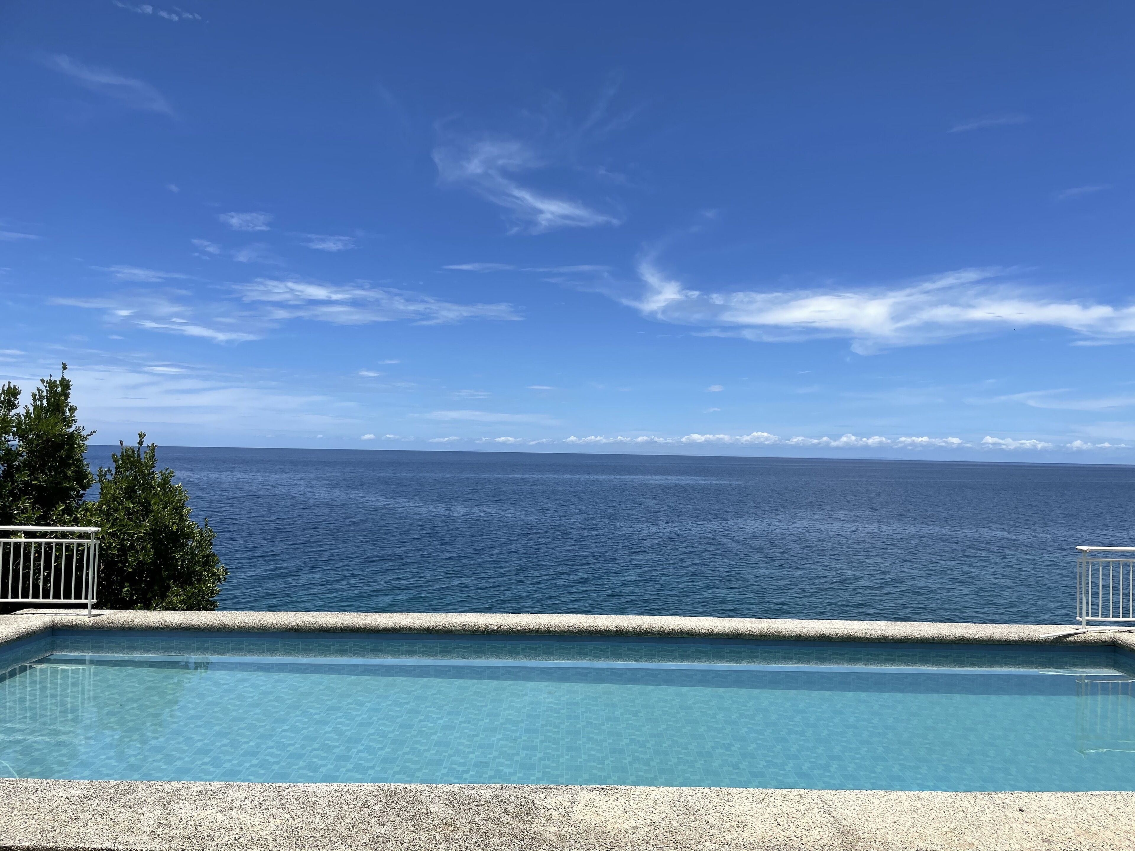 Un cielo azul despejado, mar tranquilo y piscina con borde de guijarros.