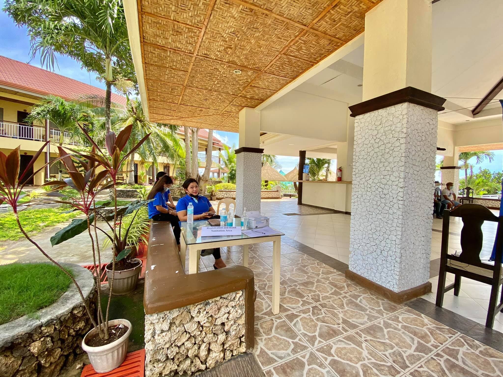 Ein Empfangsbereich mit einer Rezeption, einem Reetdach und Blick auf die umliegenden Hotelgebäude.