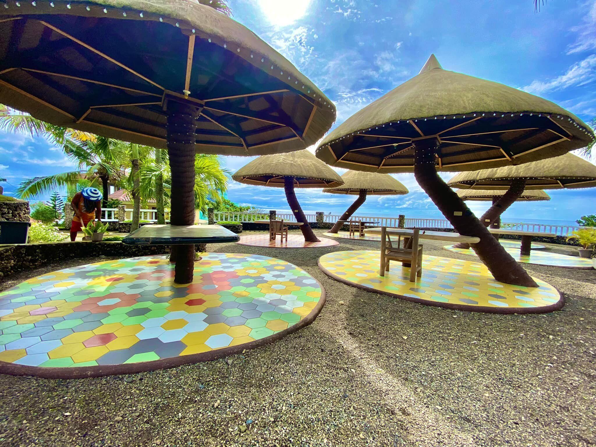 Outdoor seating areas with colorful hexagonal tiles and thatched umbrellas, overlooking a scenic view.