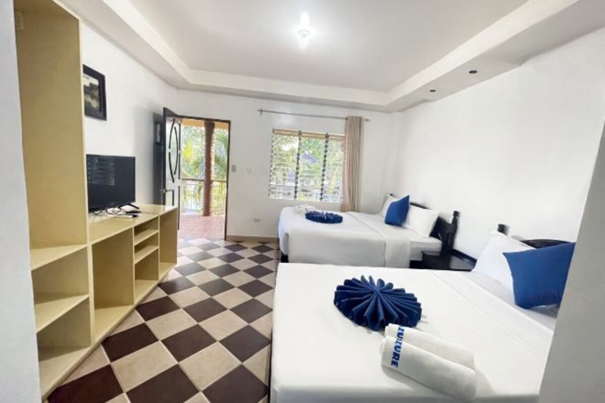 Quarto de hotel com duas camas, televisão, estante e janela com cortinas.