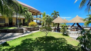 A resort with a pool area, palm trees, and a building with a red roof. - azure camotes resort hotel (San Francisco)