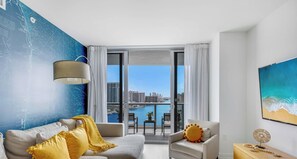 A modern living room with a sofa, armchair, and a view of a marina. - 1 Near Beach 1BR Stylish Apartment. (Hallandale Beach)