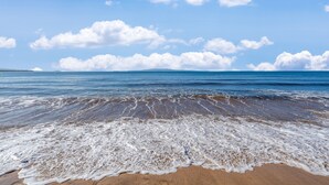Una playa con olas mansas lamiendo la orilla bajo un cielo despejado.