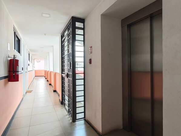 Un pasillo con un extintor, una reja metálica y un ascensor.